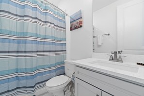 A bathroom with a striped shower curtain, a toilet, a sink with a mirror, and a towel rack.