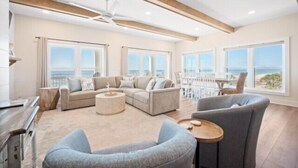 A spacious living room with a large sofa, a round coffee table, and a view of the ocean through large windows. - Grand new construction, gulf front, private pool, elevator, pet friendly! (Port Saint Joe)