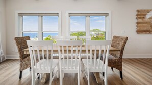 A dining area with a white table and chairs, large windows with a view of greenery and a body of water, and wooden beams on the ceiling. - Grand new construction, gulf front, private pool, elevator, pet friendly! (Port Saint Joe)