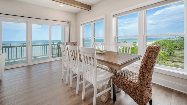 A dining area with a wooden table and white chairs, large windows with a view of the ocean, and a balcony with a railing. - Grand new construction, gulf front, private pool, elevator, pet friendly! (Port Saint Joe)