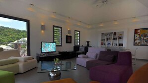 Ett modernt vardagsrum med en platt-TV, ett soffbord i glas och en bokhylla.