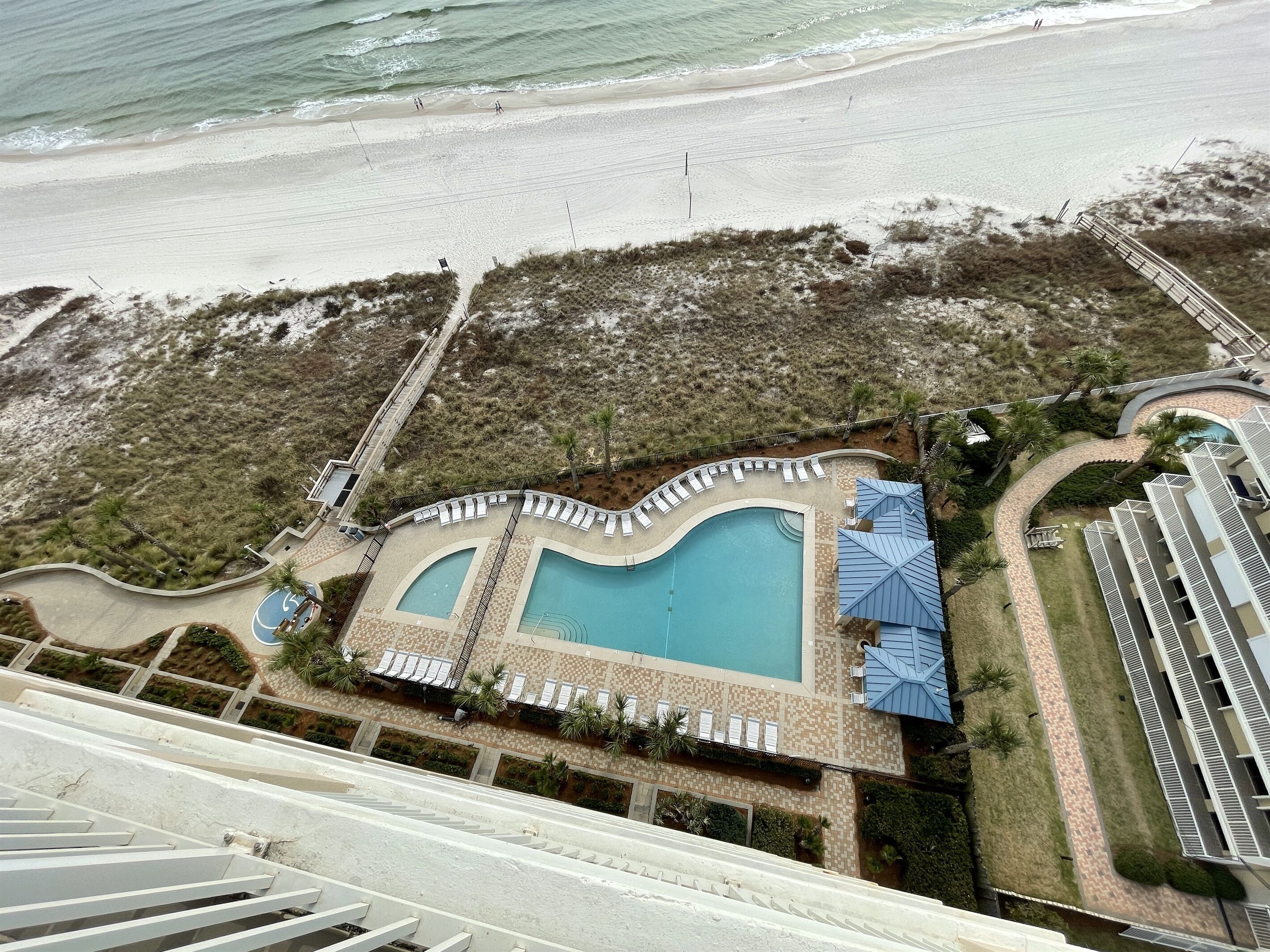 An aerial view of a resort with a large pool, beach access, and a bridge connecting to the beach.