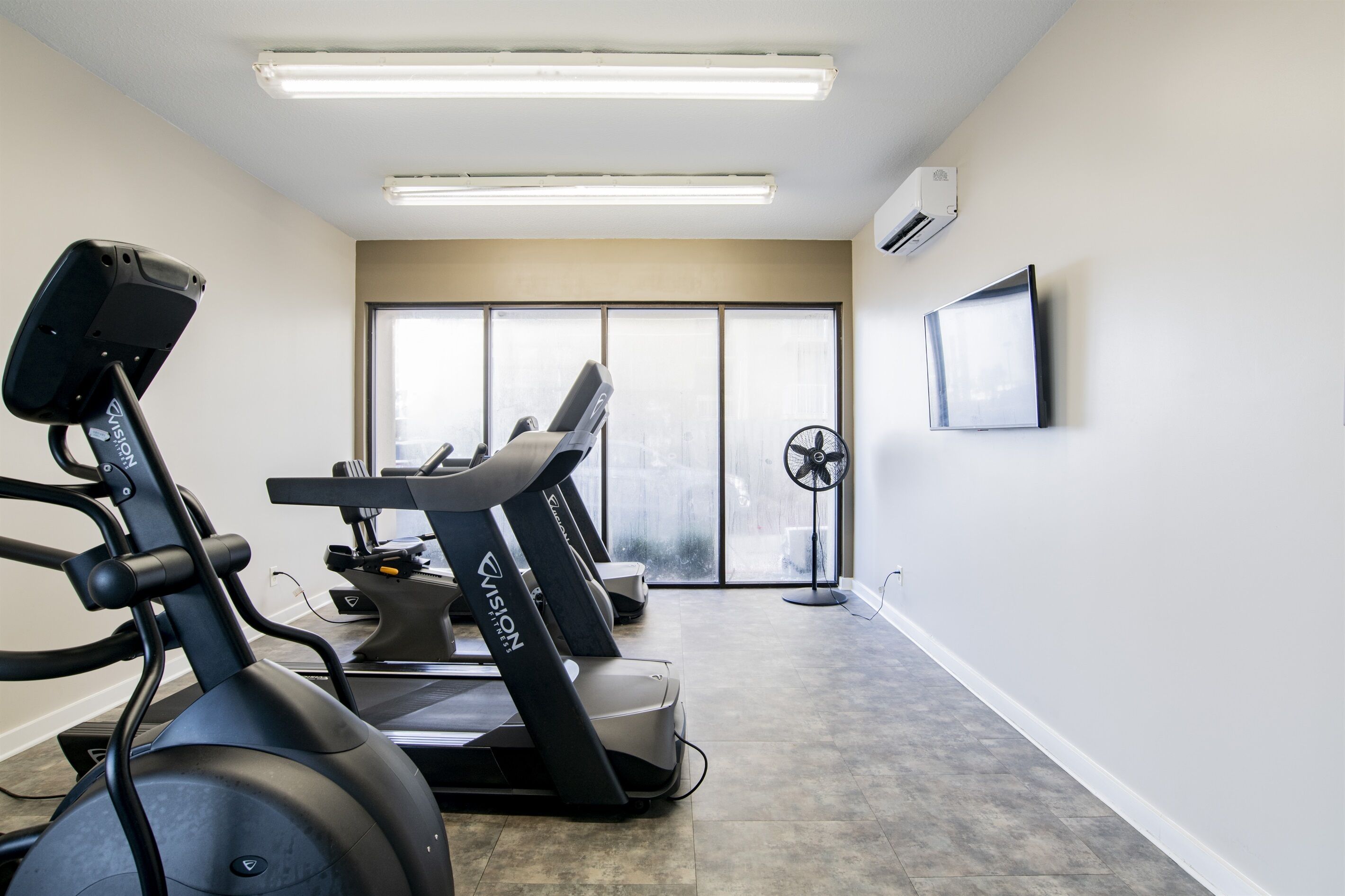 Un gimnasio con cintas de correr, una bicicleta estática y un ventilador.