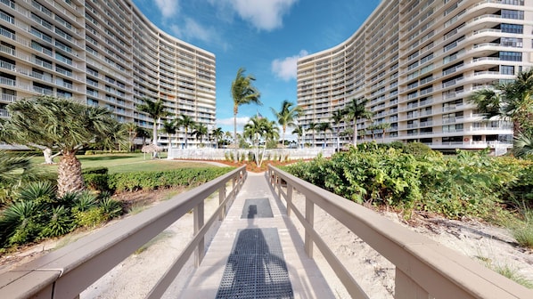 A modern hotel with a central pathway leading to a pool, surrounded by lush greenery and palm trees.