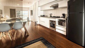 A modern kitchen with a black refrigerator, stainless steel appliances, and a dining area with a glass table and chairs.