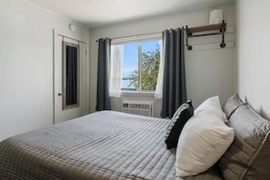 A bedroom with a bed, a window with curtains, a radiator, and a shelf with a cup.