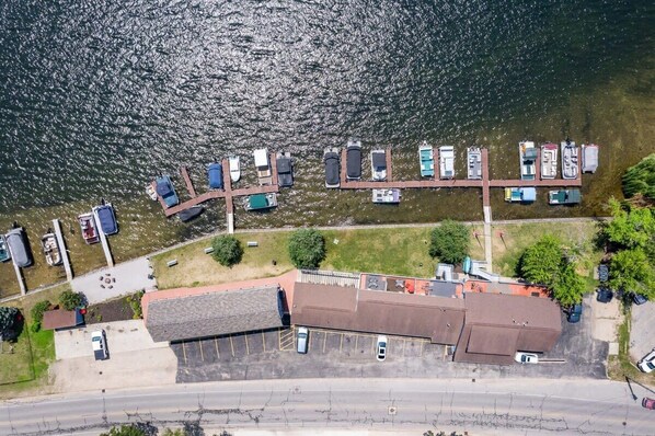 Vista aérea de un puerto deportivo con barcos amarrados a lo largo de un muelle, un estacionamiento y un edificio con techo inclinado.