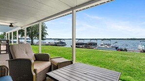 A covered outdoor area with wicker furniture, a table, and a view of boats on the water.