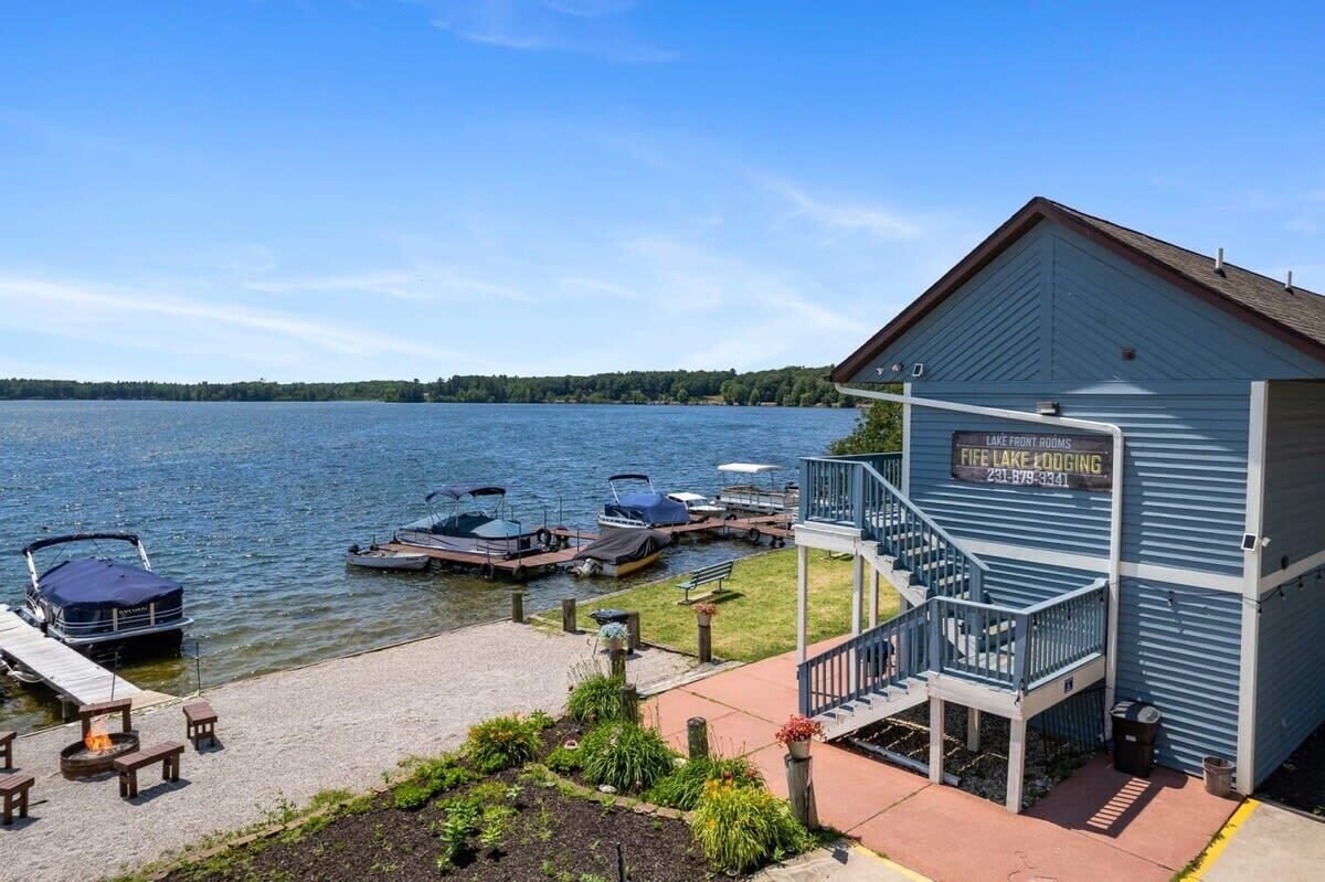 Una cabaña junto al lago con barcos amarrados, una terraza techada y un letrero que indica servicios de alojamiento y restauración.