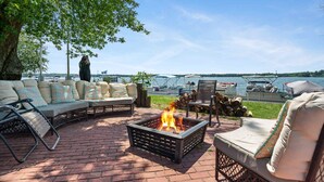 An outdoor seating area with a fire pit, cushioned seating, and a view of boats on a lake.