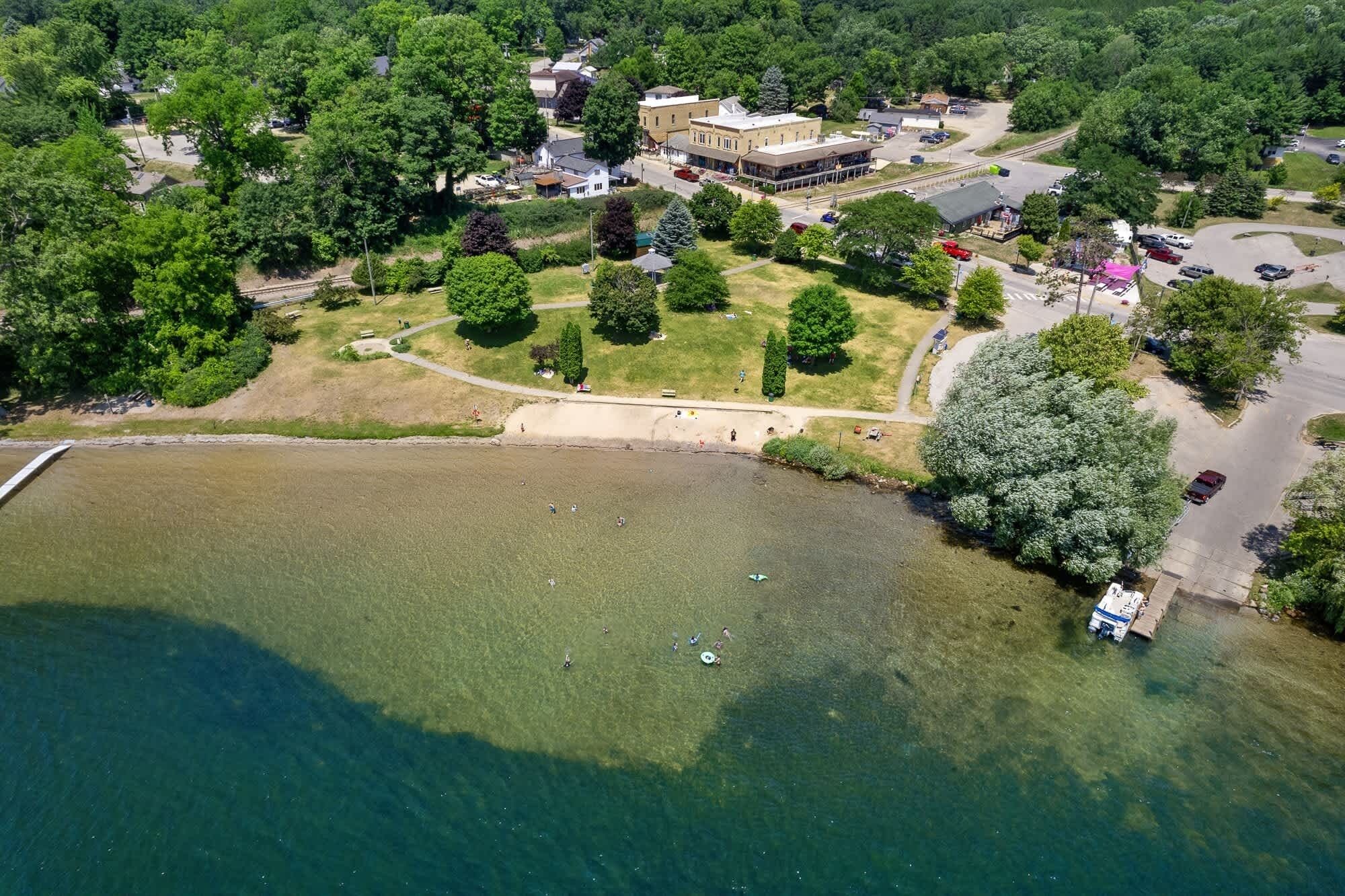 An aerial view of a lakeside area with a park, buildings, and a dock.