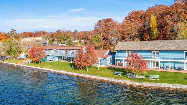A waterfront hotel with multiple buildings, a grassy area with benches, and trees with autumn foliage.