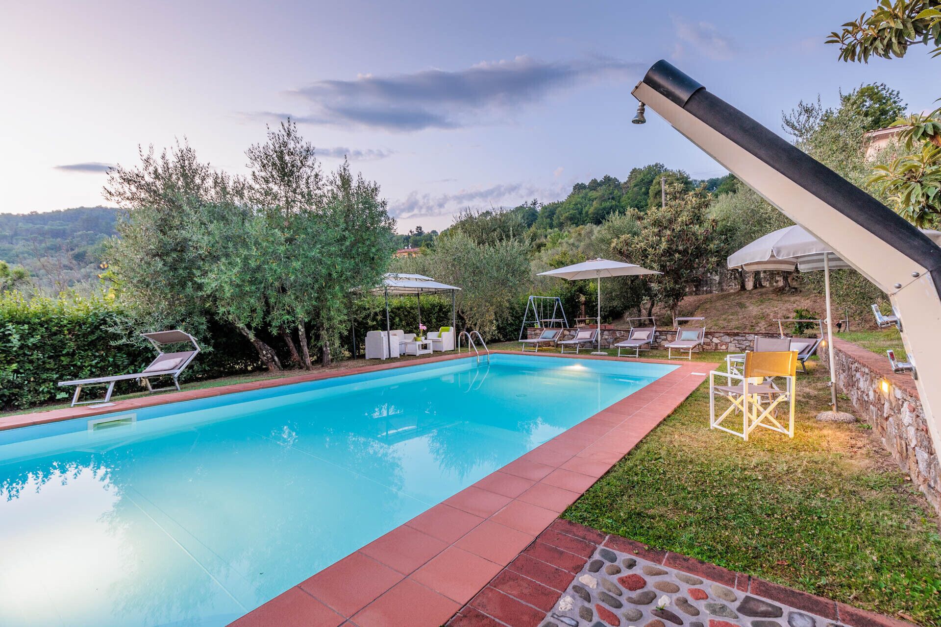 Une piscine entourée de verdure et de collines, avec des chaises longues et des parasols.