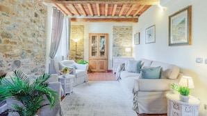 A cozy living room with a stone wall, wooden ceiling beams, a fireplace, and a dining area with a cabinet. - Villa Dondolino, a Stylish Farmhouse with Private Pool close to Lucca and the Beach (Lucca)