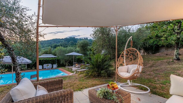 A poolside area with wicker furniture, a hanging chair, and a table with fruit. - Villa Dondolino, a Stylish Farmhouse with Private Pool close to Lucca and the Beach (Lucca)