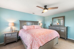 A bedroom with a bed, two nightstands, a dresser, a ceiling fan, and a mirror.