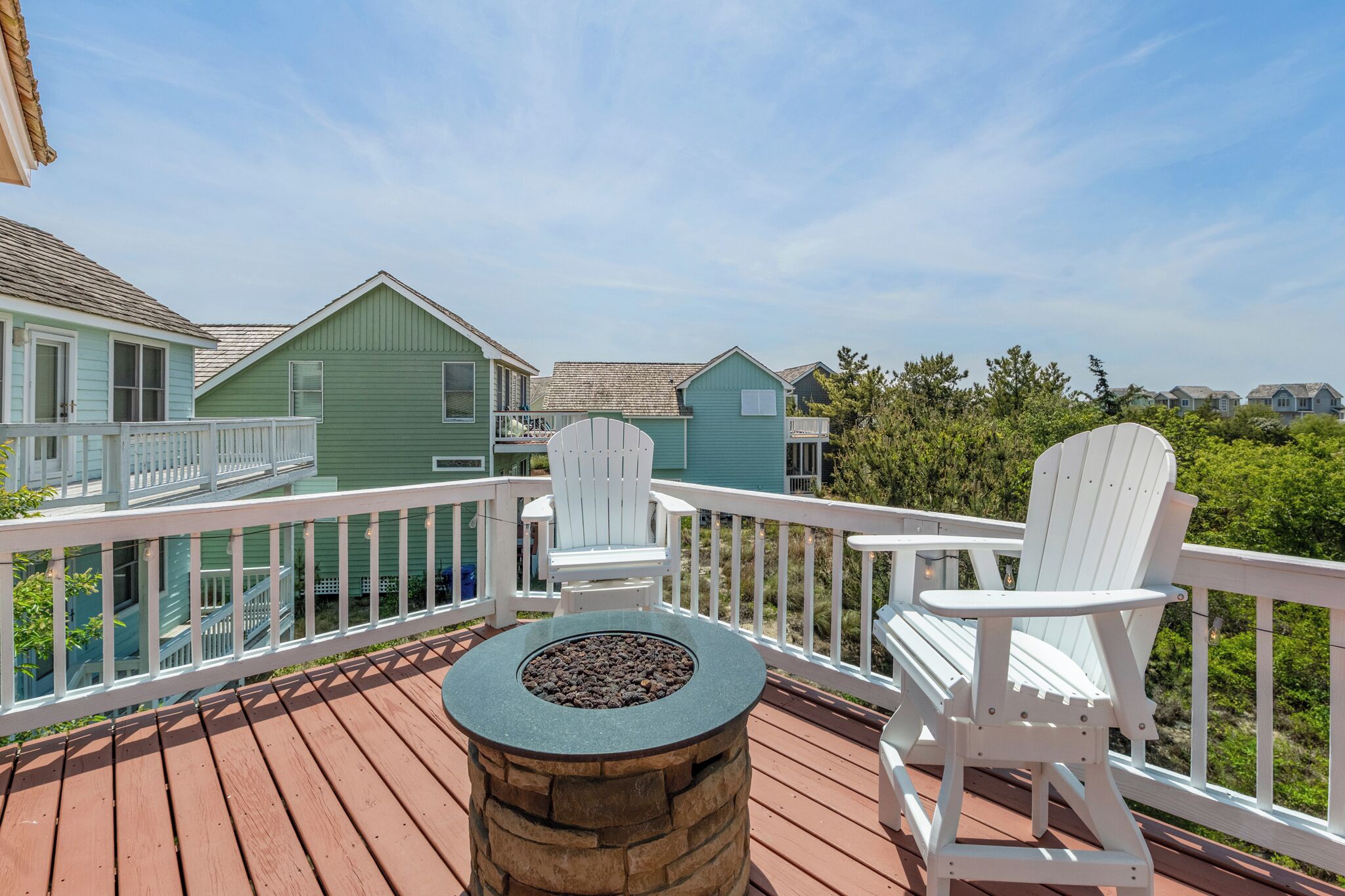 A wooden deck with two Adirondack chairs and a round table with a fire pit.