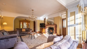 Een ruime woonkamer met een open haard, banken en een kroonluchter.
