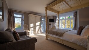 Een slaapkamer met een hemelbed, een zithoek met een fauteuil en een kledingkast.