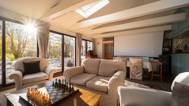 Een gezellige woonkamer met een groot raam, een bank, een salontafel met een schaakspel en een televisie.