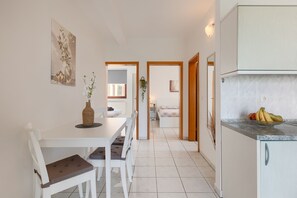 A modern kitchen with white cabinets, a dining area with a white table and chairs, and a hallway leading to a bedroom.