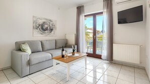 A modern living room with a grey sofa, a wooden coffee table, a TV mounted on the wall, and a sliding glass door leading to an outdoor area. - Beautiful spacious apartment (No. 1) with 2 bedrooms 300m to the beach (Poreč)