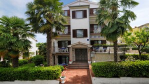 A multi-story building with a central entrance, surrounded by lush greenery and palm trees. - Beautiful spacious apartment (No. 1) with 2 bedrooms 300m to the beach (Poreč)