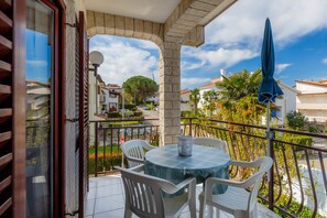 A balcony with a table and chairs, a blue umbrella, and a view of the street and buildings.