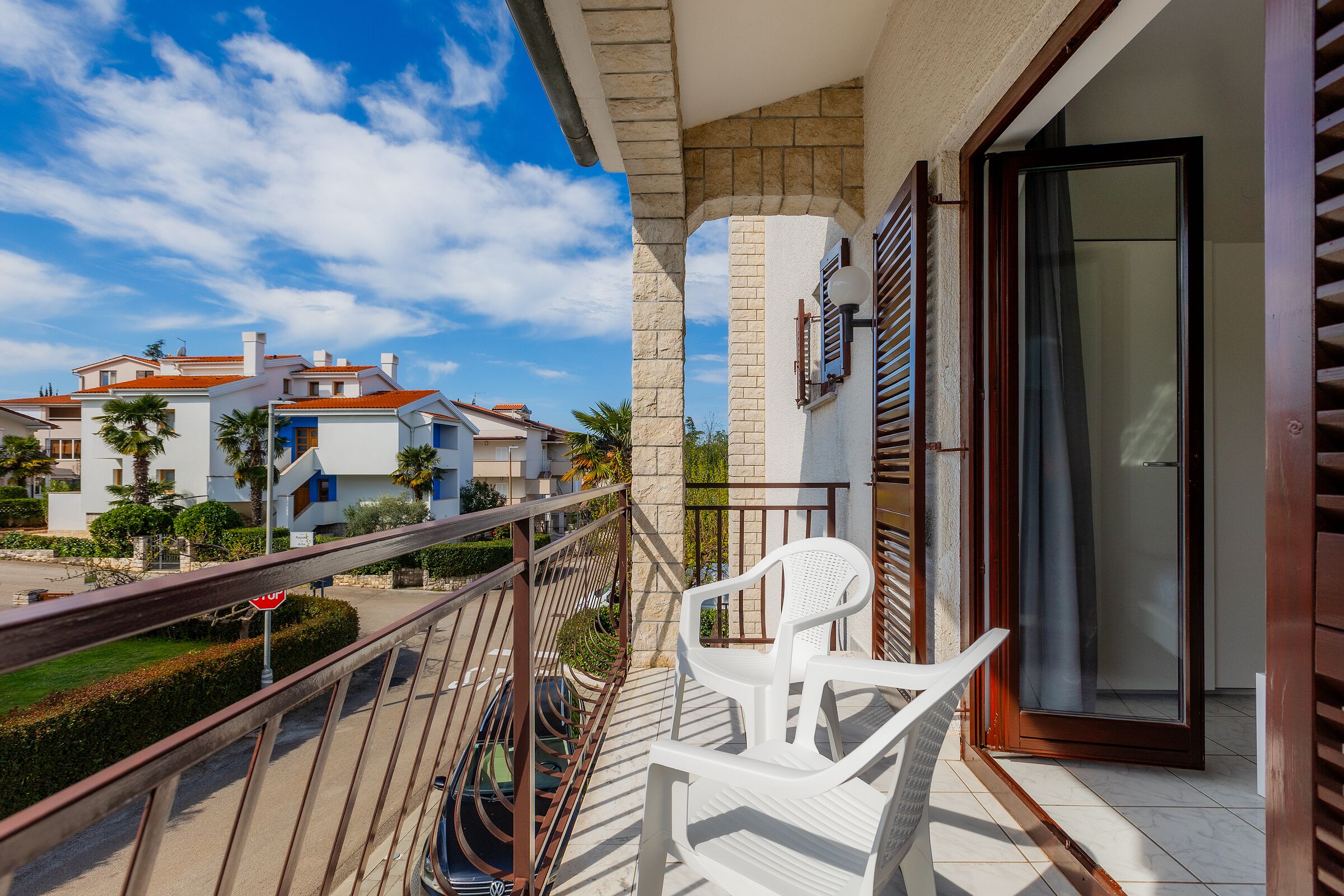 A balcony with a white chair, a stop sign, and a view of neighboring buildings.