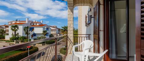 A balcony with a white chair, a stop sign, and a view of neighboring buildings.
