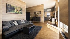 Ein modernes Wohnzimmer mit einem dunkelgrauen Sofa, einem schwarzen Couchtisch und einem großen Gemälde einer Seenlandschaft.