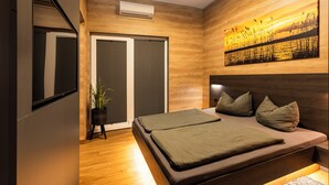 Ein modernes Schlafzimmer mit einem großen Bett, einer Schiebetür, einer Zimmerpflanze und einem Sonnenuntergangsbild an der Wand.