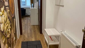 Um corredor com piso de madeira, um radiador, uma pequena mesa e uma prateleira fixada na parede.