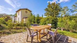 A patio with a wooden table and chairs, surrounded by greenery and a building in the background. - Country House with heated pool near the center (Firenze)