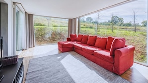 A modern living room with a red sectional sofa, large windows, and a view of a green landscape. - Country House with heated pool near the center (Firenze)