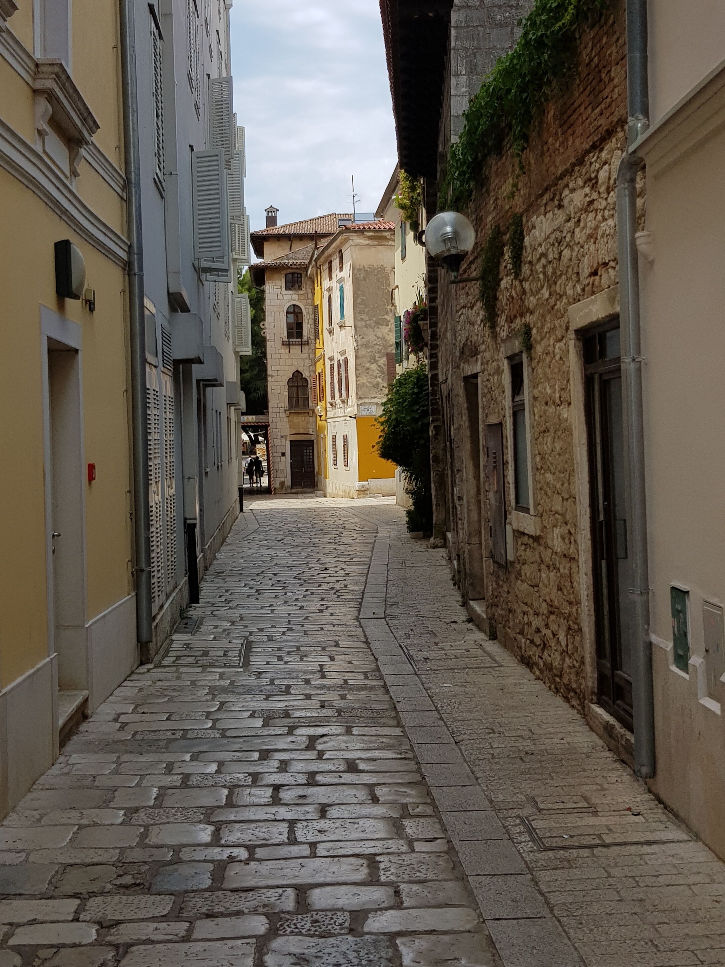 A narrow cobblestone street flanked by historic buildings with stone facades and traditional architecture.