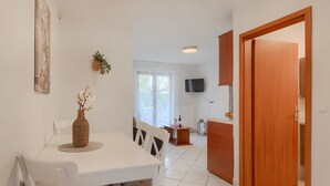 A clean, modern room with a dining table, chairs, a TV, and a wooden door. - Beautiful spacious apartment (No. 5) with 2 bedrooms 300m from the beach (Porec)
