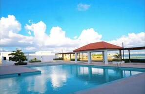 Relax by the serene pool surrounded by a shaded pavilion and lush greenery.
