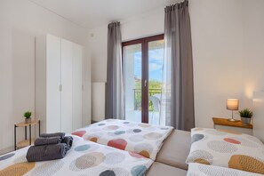 Une chambre à coucher avec un lit, une table de chevet avec une lampe, une plante en pot et une vue sur l’extérieur.