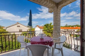 Un balcon avec une table et des chaises, un parasol bleu et une vue sur des bâtiments et de la verdure.