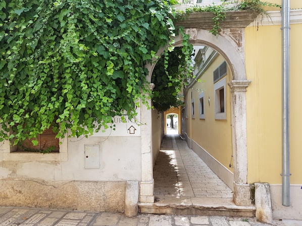 A narrow alleyway with a stone archway, a sign indicating a restaurant, and a yellow building on the right.