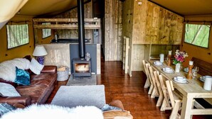 Interior acogedor de una cabaña con un estufa de leña central, un comedor con sillas de madera y una sala de estar con un sofá de cuero marrón y cojines mullidos.