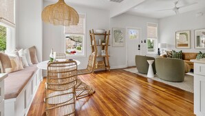 A bright, open living area with a wooden floor, a wicker chair, a round table, and a sofa with cushions. - Prime Location in Park Circle | The Aloha Cottage (North Charleston)