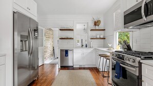 A modern kitchen with white cabinetry, stainless steel appliances, and wooden flooring. - Prime Location in Park Circle | The Aloha Cottage (North Charleston)