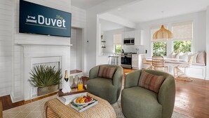 A modern living room with a fireplace, comfortable seating, a dining area, and a kitchen in the background. - Prime Location in Park Circle | The Aloha Cottage (North Charleston)