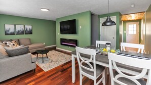 A living room with a grey sofa, a flat-screen TV, and a fireplace. - Large 3 floor Townhome with Patio, Backyard and Sauna (Manchester)