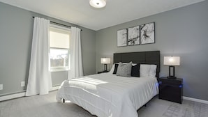 A bedroom with a large bed, two bedside tables with lamps, a window with curtains, and artwork on the wall. - Large 3 floor Townhome with Patio, Backyard and Sauna (Manchester)