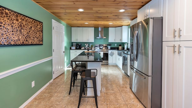 A modern kitchen with white cabinets, stainless steel appliances, a wooden ceiling, and a green accent wall. - Large 3 floor Townhome with Patio, Backyard and Sauna (Manchester)