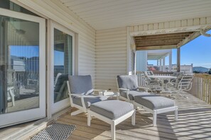 Un espacio al aire libre techado con mobiliario blanco, que incluye sillas y una mesa, y vistas al océano.
