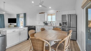 A modern kitchen with white cabinets, stainless steel appliances, wicker chairs, and a round dining table. - The Shady Lady: Spacious Ocean View Home with Open Floorplan (Oak Island)